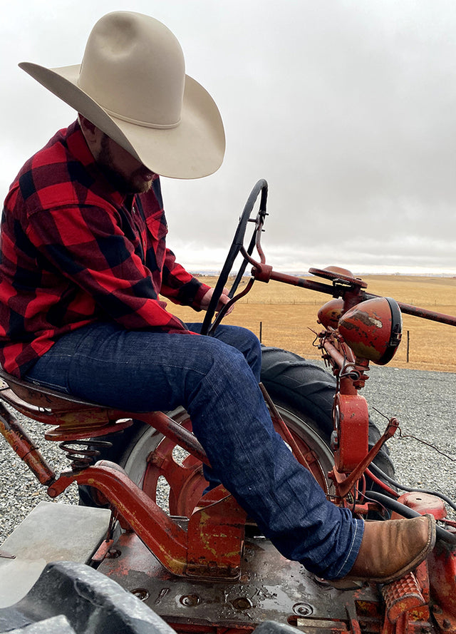 A man sitting on a tractor in a red buffalo plaid men's heavyweight flannel shirt