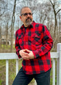 A man leaning against a fence in a red buffalo plaid men's heavyweight flannel plaid shirt