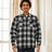 A man stands in front of the curtains in a black white men's fleece lined flannel shirt jacket